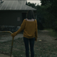 A woman facing away from the camera looks toward a roadside rest stop building that appears to be abandoned in horror short Seek.